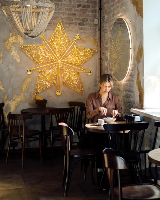 Achtzackiger goldener Wandstern von Alganic in urbanem Café – dekorative Lichtskulptur mit ruhiger, stimmungsvoller Präsenz.