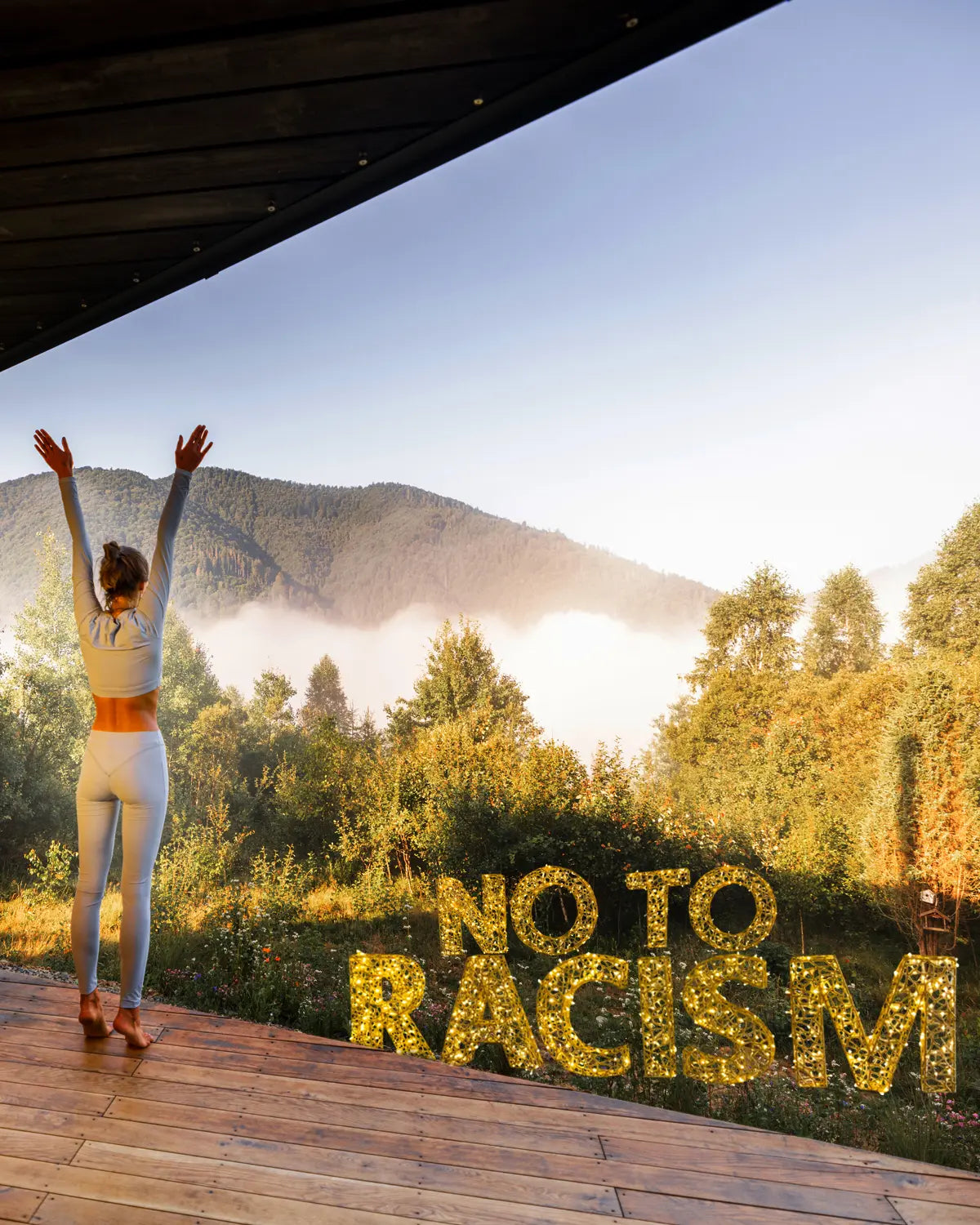 Lichtinstallationen mit der Aufschrift „NO TO RACISM“ aus goldenen Buchstaben – als kraftvolles Zeichen in einer morgendlichen Landschaftsszene.