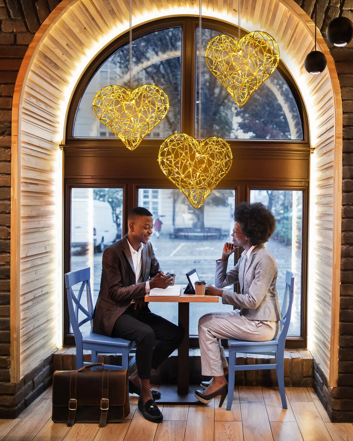 Drei goldene Alganic-Herzobjekte als Lichtinstallation im Fenster eines Cafés – stilvolle Rauminszenierung mit warmer Atmosphäre.
