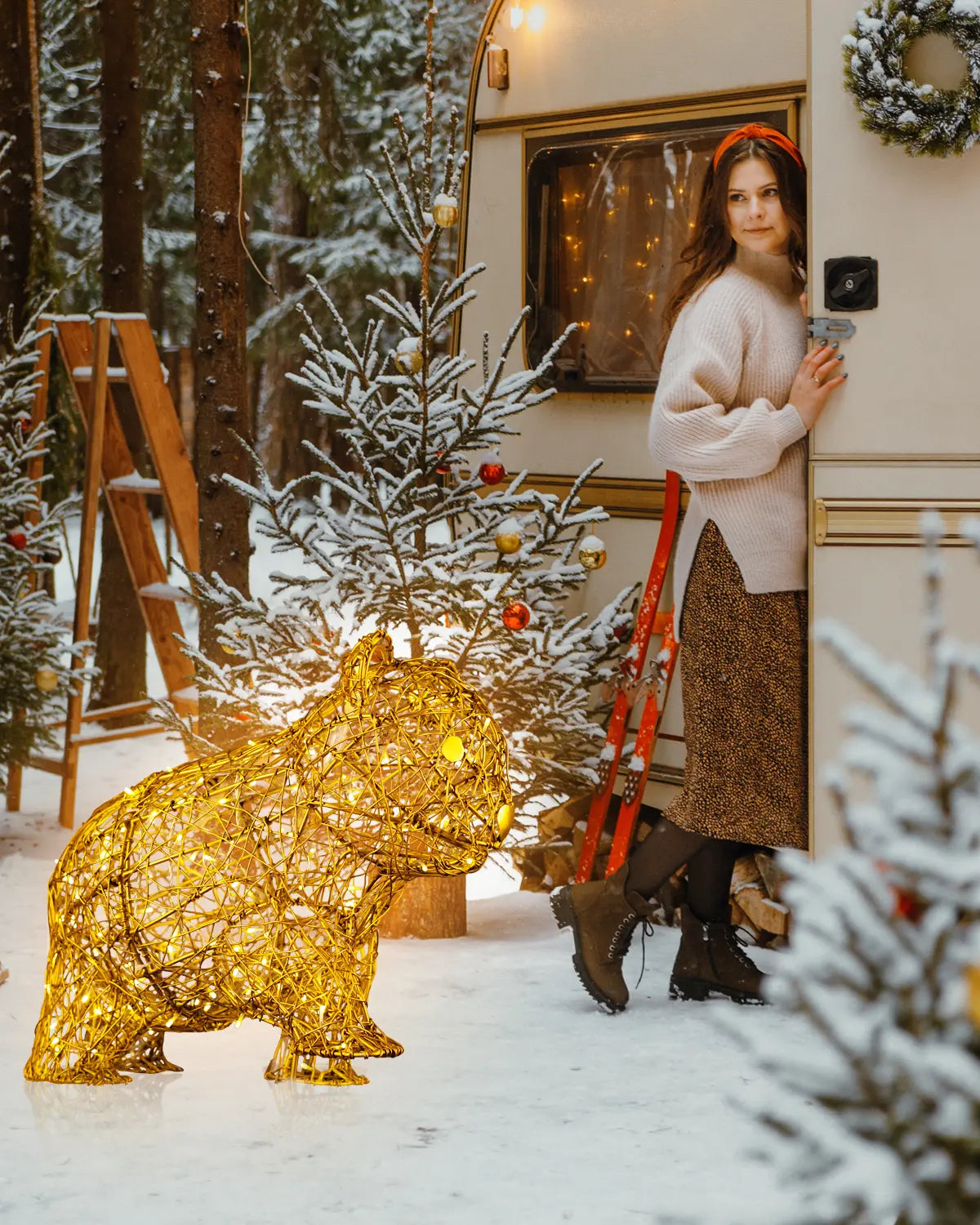 Goldenes Lichtobjekt in Form eines Wombats vor verschneitem Wohnwagen – weihnachtliche Waldszenerie mit geschmückten Tannenbäumen und nostalgischer Stimmung.