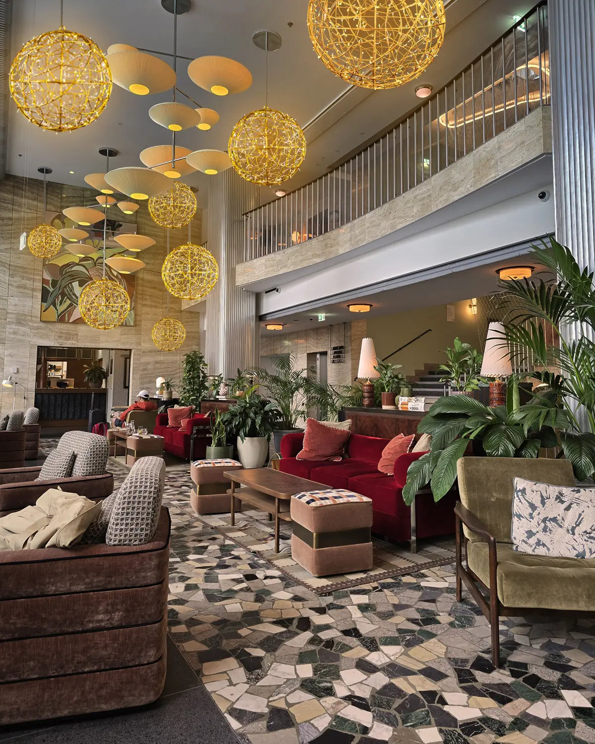 Moderne, stilvolle Lobby eines Hotels mit hängenden Kugelleuchten aus goldenem Draht, samtigen Sesseln und vielen Pflanzen.