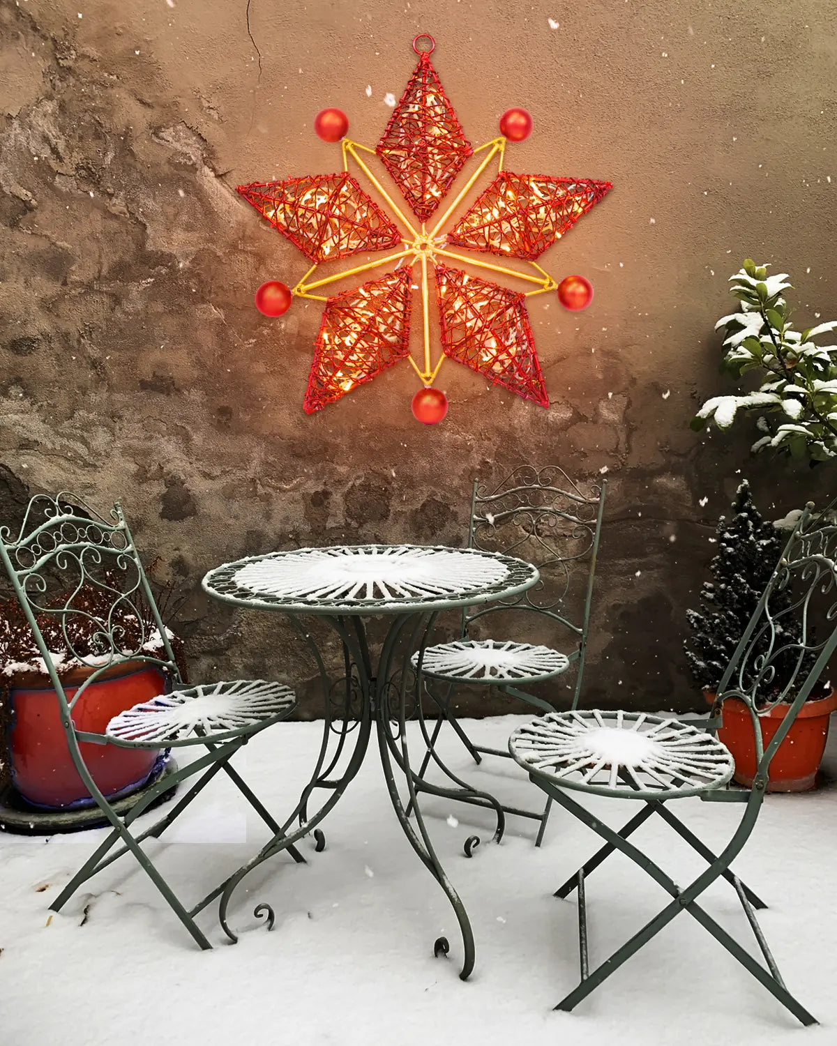 Leuchtstern in Rot und Gold an verschneiter Mauer – Alganic-Wandobjekt über winterlichem Café-Ensemble im Innenhof.