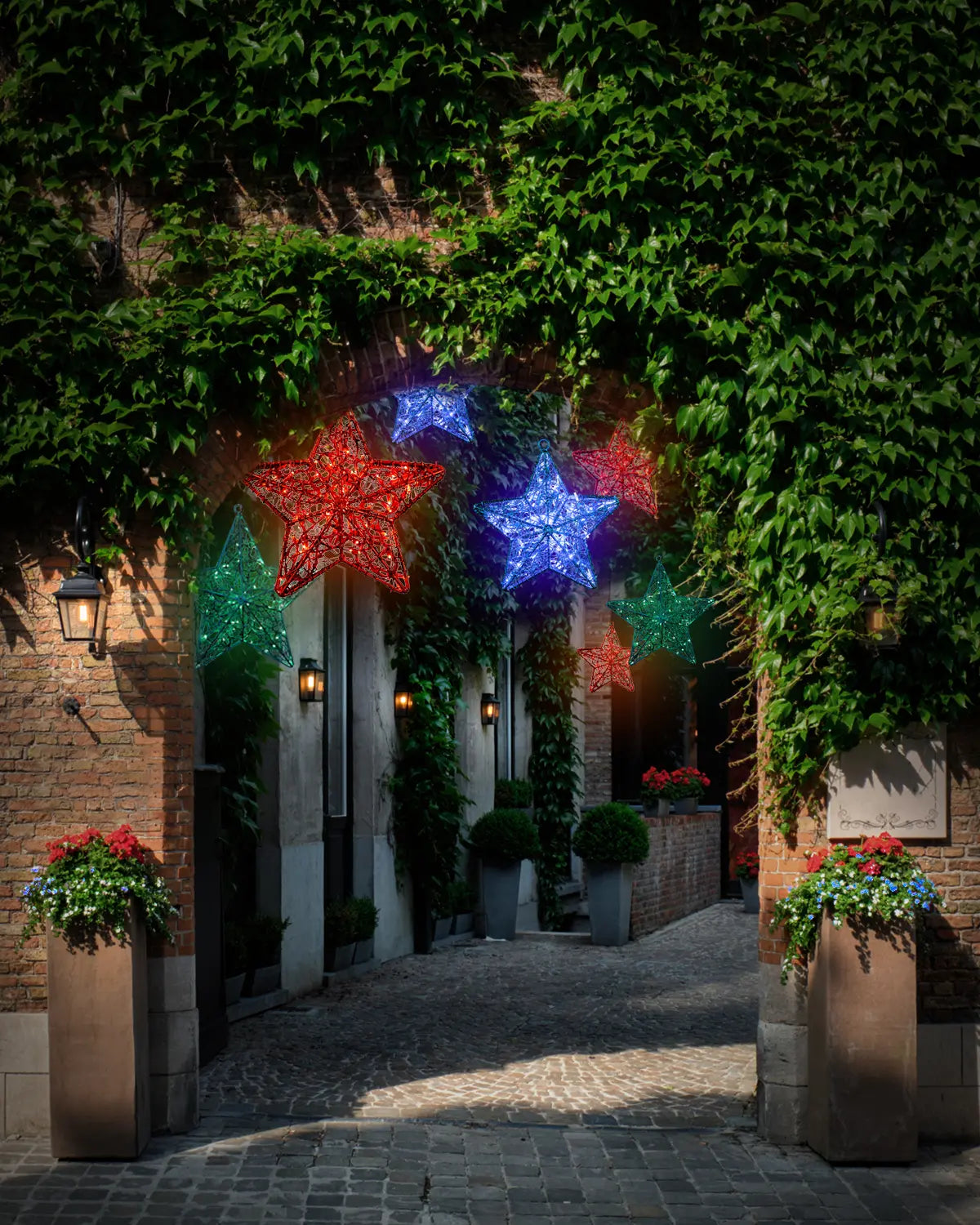 Hängende Lichtobjekte in Sternform in Rot, Blau und Grün – festliche Installation in einem begrünten Torbogen eines historischen Innenhofs.