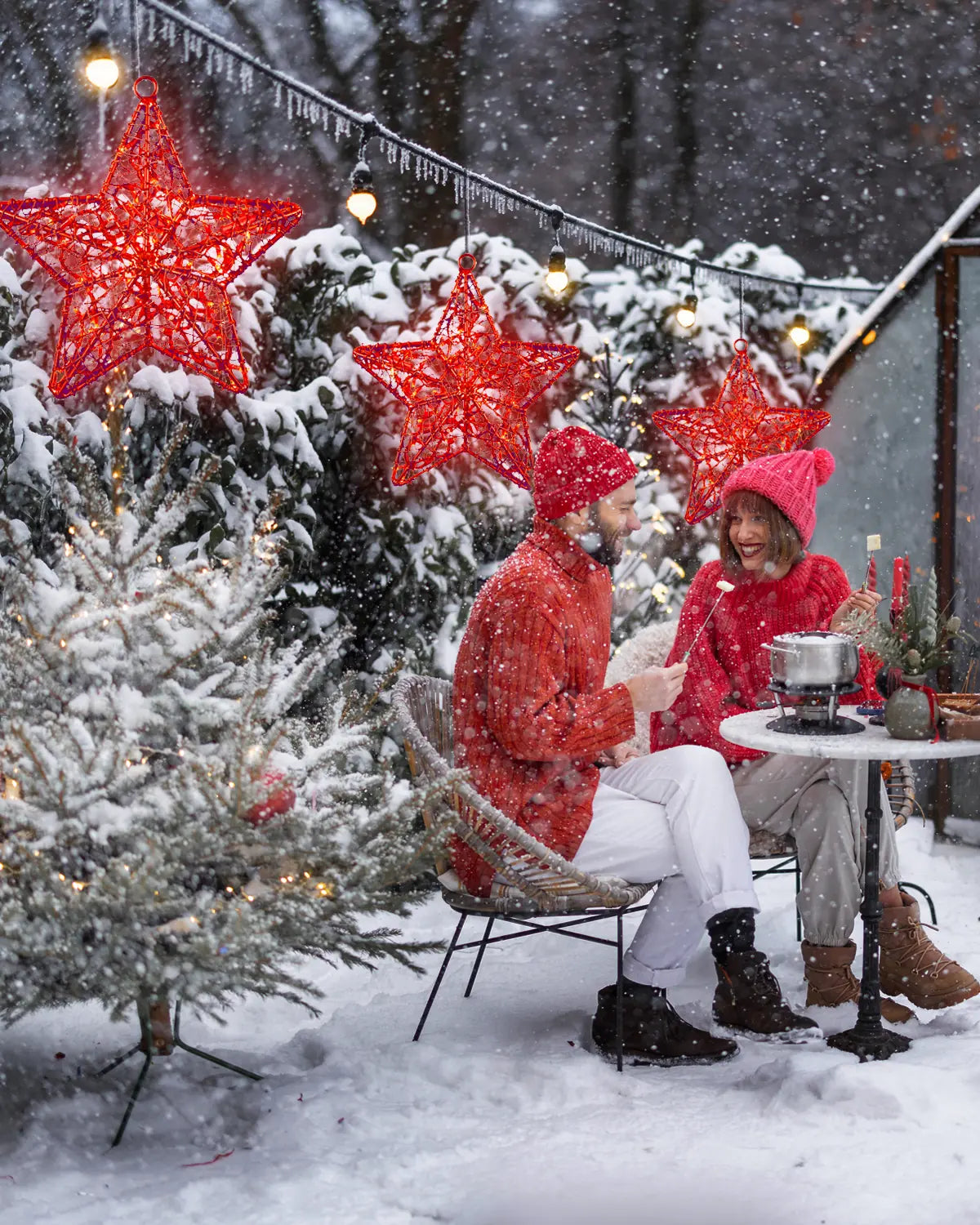 Rote Alganic-Sterne über verschneitem Wintergarten – festliche Lichtszenografie für Außenbereiche mit Fondue und Frost.